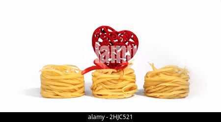 Essen zum Valentinstag. Italienische Pasta. Spaghetti Capellini, mit einem kreativen roten Herz mit einer Schleife, isoliert auf einem weißgrauen Hintergrund, mit hartem Sha Stockfoto