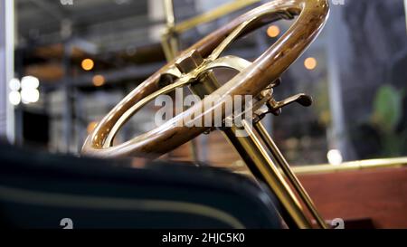 Nahaufnahme der Oldtimer-Details auf der Messe. Retro-Cabriolet und der goldene Lenkmechanismus mit einem polierten Holzrad. Stockfoto