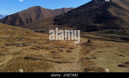 Schöne Luftaufnahme der hügeligen Berglandschaft verlassene Hauswracks. Ruinen eines alten Backsteingebäudes auf einem gelben Hang von Herbstmontagen. Stockfoto