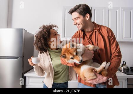 Aufgeregt interracial paar Blick auf einander in der Nähe lustige shiba inu Hund Stockfoto