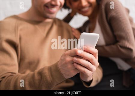 Beschnittene Ansicht eines multiethnischen Paares mit Smartphone zu Hause Stockfoto
