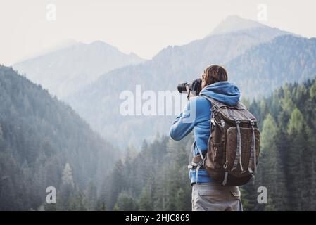 Junger, fröhlicher Fotograf, der mit einer Digitalkamera in einem Gebirge fotografiert. Reise- und Active Lifestyle-Konzept Stockfoto