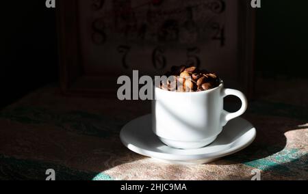 Kaffeebohnen in einer weißen Keramikschale auf einem dunklen Hintergrund mit harten Schatten Nahaufnahme Punkt, wenn Ansicht Stockfoto