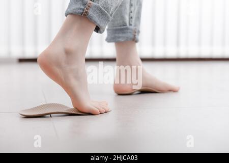 Frau, die orthopädische Innensohle innen anpasst, Nahaufnahme. Mädchen, das zu Hause eine Innensohle neben dem Fuß hält. Orthopädische Einlagen. Banner zur Fußpflege. Flache Füße Stockfoto