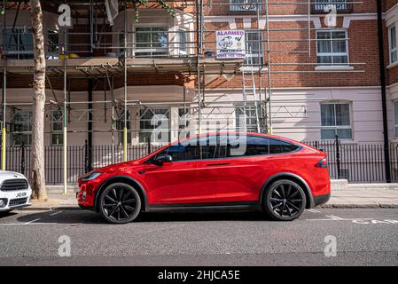 Rotes, modernes Tesla-Auto, das an der Straße in der Stadt durch Gebäude geparkt wurde Stockfoto