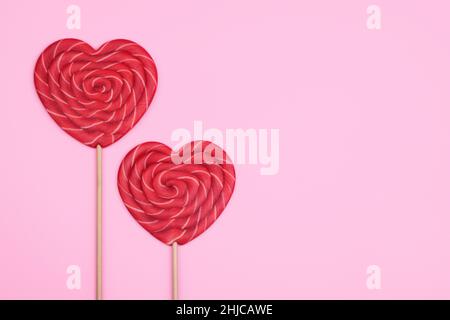 Zwei große rote herzförmige Lutscher auf einem rosa Hintergrund. Das Konzept des Valentinstag. Stockfoto