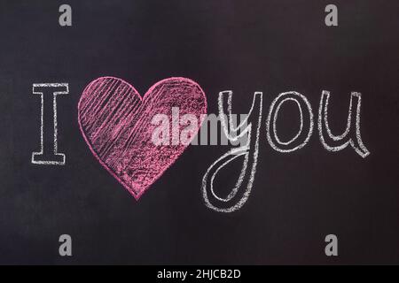 Handgeschriebene Kreidebeschriftung auf der Tafel 'I love you' und ein rotes Herz. Weihnachtsschriftzug zum Valentinstag. Stockfoto