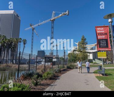 Los Angeles, CA, USA - 26. Januar 2022: Zwei Menschen laufen am La Brea Tar vorbei, während Turmdrehkrane über der neuen Baustelle von LACMA in Los Angel stehen Stockfoto