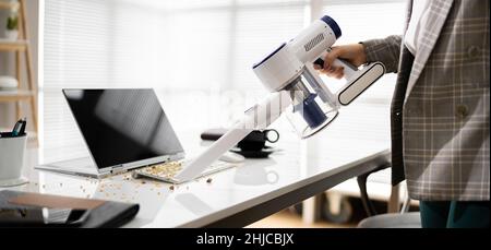 Reinigung Des Büroschreibtisches Mit Einem Kabellosen Staubsauger Stockfoto