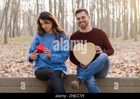 Junges Paar, das den valentinstag feiert und sich gegenseitig ein Geschenk in einem Park schenkt Stockfoto