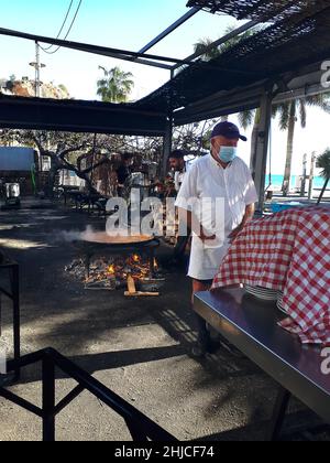 Kochen einer Paella in einer riesigen Eisenpfanne am Strand von Burriana in Nerja an der Costa del Sol in Südspanien. Sie wird aus Reis, Huhn und Garnelen hergestellt Stockfoto