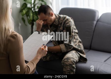 Deprimierter junger Militärmann, der während der Therapiestunde auf dem Sofa sitzt Mit Psychologen Stockfoto