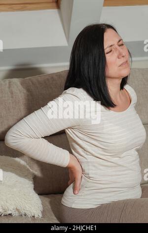 Ältere Frau mittleren Alters, die zu Hause an Rückenschmerzen und Flankenschmerzen leidet. Muskelprobleme, Nierensteine oder Gallenblasenerkrankungen. Symptome von Krankheit o Stockfoto