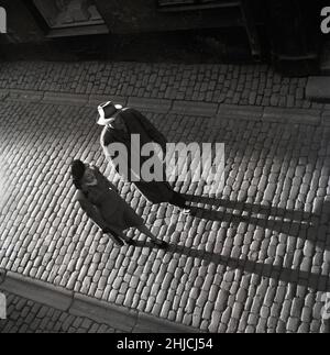 1940s Paar. Der Mann und die Frau, die in einer alten Straße spazieren, werfen lange Schatten, wenn die Abendsonne auf sie scheint. Schweden 1946. Foto Kristoffersson Y6-2 Stockfoto