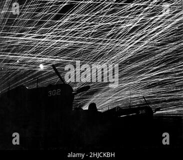 Japanische Nachthemd-Raider werden von den Marine-Verteidigern des Flugplatzes Yontan auf Okinawa mit einem Luftabwehrfeuer begrüßt. Im Vordergrund stehen die marinen Kampfflugzeuge der Staffel „Hell's Belles“. Ca. 1945. Stockfoto