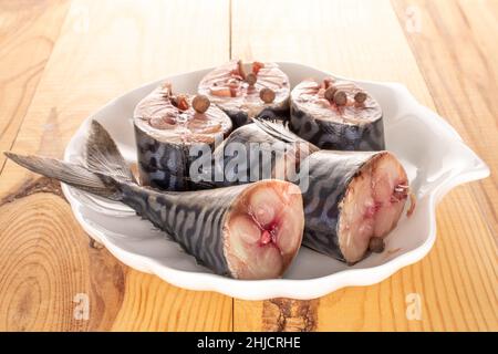 Mehrere Stücke gesalzener Makrele auf einer weißen Keramikplatte auf einem Holztisch, Makro. Stockfoto