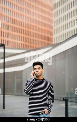 Junger Mann, der auf einem roten Smartphone auf der Straße läuft und spricht Stockfoto