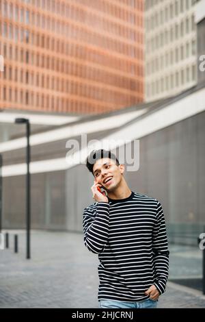 Junger lächelnder Mann, der auf einem roten Smartphone auf der Straße läuft und spricht Stockfoto