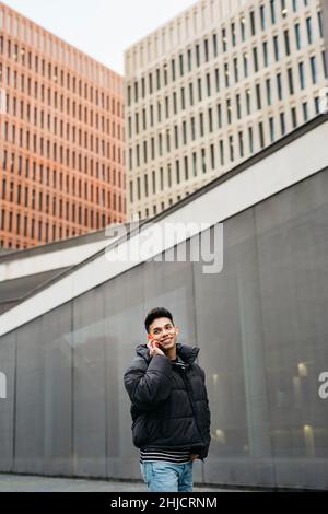 Junger Mann, der auf einem roten Smartphone auf der Straße läuft und spricht Stockfoto