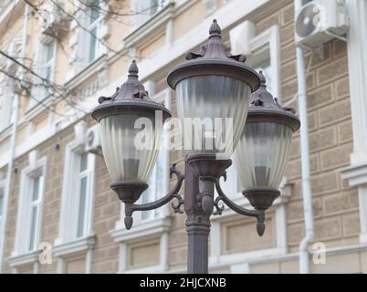 Eine Stange mit tagsüber ausgeschalteten Straßenlaternen und einem Gebäude im Hintergrund. Stockfoto