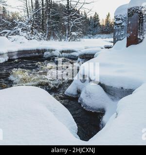 Wasserfluss eines kleinen schneebedeckten Waldflusses, Eisfragmente aus der Nähe. Langzeitbelichtung. Konzept der globalen Erwärmung, Ökologie, Umweltschutz, g Stockfoto