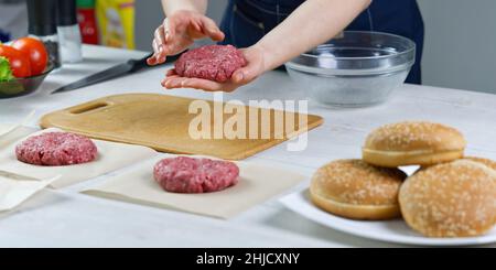 Die Hand einer Frau formt ein Rindfleisch für eine Hamburger-Party. Portionieren von gemahlenem Fleisch. Hausgemachte Burger. Lebensmittel zu Hause machen. Stockfoto