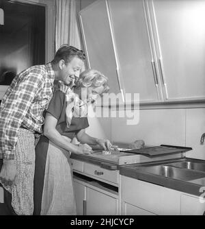 In der Küche im 1950s. Ein junges Paar, das herzförmige Lebkuchenkekse für weihnachten backen soll. Sie legt die herzförmige Metallform auf den Teig, um die Form zu machen. Sie ist die Schauspielerin UllaCarin Rydén. Schweden 1951. ref Kristoffersson BE65-9 Stockfoto