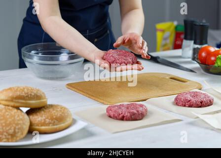 Die Hand einer Frau formt ein Rindfleisch für eine Hamburger-Party. Portionieren von gemahlenem Fleisch. Hausgemachte Burger. Lebensmittel zu Hause machen. Stockfoto