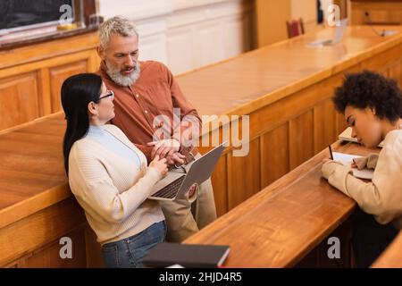 Asiatische Student im Gespräch mit reifen Lehrer in Auditorium der Universität Stockfoto