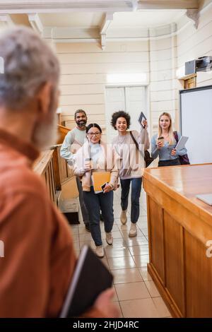 Interracial Studenten mit Geräten und Kaffee zu gehen Blick auf verschwommene Lehrer in der Universität Stockfoto