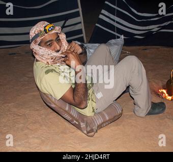 Ein Araber sitzt auf einem Stuhl in der Wüste neben einem Lagerfeuer Stockfoto