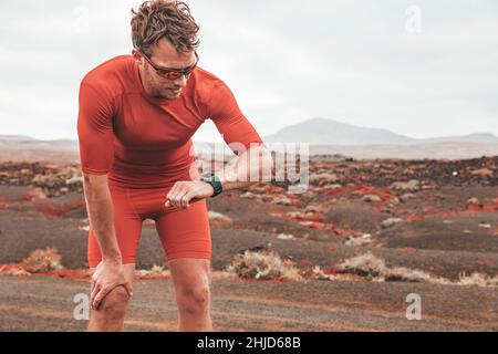 Müde Läufer Mann Überprüfung tragbare Technologie Sport Smartwatch während des Outdoor-Trainings. Sportlerin, die beim Training auf dem Wüstenpfad auf die Uhr schaut Stockfoto