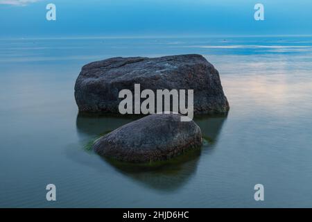 Blaue Stunde nach dem Sonnenuntergang über der felsigen Ostsee kosten. Kleine Steine und große Felsbrocken im Meer. Langzeitbelichtung Stockfoto