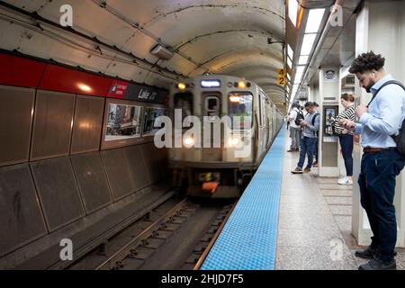 Passagiere, die auf Telefone herabblicken, während der Zug auf einem langen Bahnsteig auf der roten Linie cta Lake Station anfährt, der längsten in Nordamerika chicago illinois Stockfoto