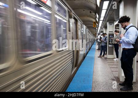 Passagiere, die nach unten auf Telefone blicken, während der Zug auf einem langen Bahnsteig auf der roten Linie cta Lake Station vorbeifährt, der längsten in Nordamerika chicago illinois Einheit Stockfoto