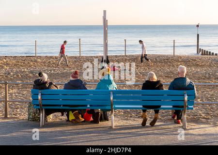 Menschen, die auf einer Bank sitzen und ein Strandvolleyball-Spiel beobachten Stockfoto