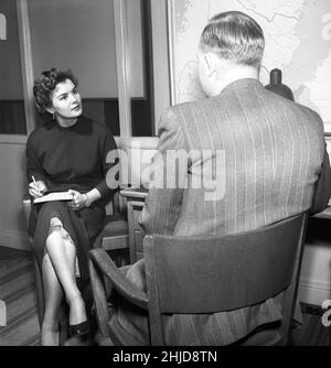 Büromädchen in den 1950s. Eine Frau sitzt mit einem Notizbuch in ihrem Schoß und schreibt Notizen von dem, was der Mann sagt, möglicherweise einen Brief, den sie später schreiben wird. Eine Sekretärin zu haben, war in der Vergangenheit häufiger als heute. Sie ist nett gekleidet und hinterlässt einen ernsthaften Eindruck. Sie hat einen Unterrock sichtbar. Schweden 1954.Foto Kristoffersson BO25-2 Stockfoto