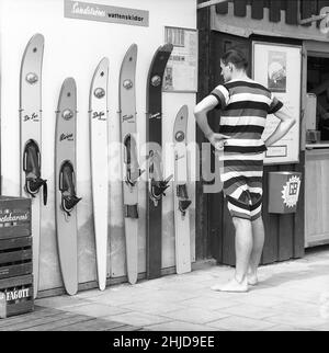 Wasserski in der 1960s. Ein junger Mann vor verschiedenen Wasserski-Modellen der schwedischen Sandströms skidfabrik. Die Modelle heißen De Lux Sport, Riviera Trick, Delfin Slalom, Florida Slalom, Champion und Bambi, die wie ein Kindermodell aussehen. Seltsamerweise trägt der Mann einen historischen männlichen Badeanzug, der Anfang des 20th. Jahrhunderts verwendet wurde. Kristoffersson Ref. CZ58-1 Stockfoto