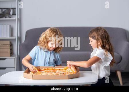 Niedliche kleine Jungen und Mädchen essen Pizza zu Hause. Kinder, die zu Hause auf der Party eine Pizza halten. Kinder teilen sich gemeinsam eine Pizza. Stockfoto