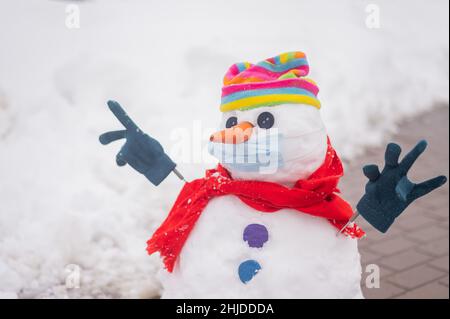 Schneemann in einem Regenbogenhut und einer medizinischen Maske. Stockfoto