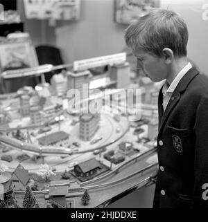 Spielzeug in der 1960s. Ein Junge an einer Modelleisenbahn in einem Geschäft. Es wurde mit Gebäuden und Bäumen gebaut und war damals ein beliebtes Hobby. Die Modelleisenbahnen im Bild sind von britischen Tri-ang-Eisenbahnen gemacht. Weitere berühmte Manufakturen waren Märklin und Fleischmann. Schweden 1962 Stockfoto