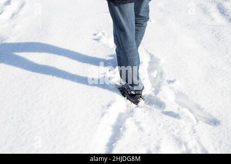 Ein Mann in Jeans und Sneakers läuft an einem Wintertag im weißen, flauschigen Schnee. Stockfoto