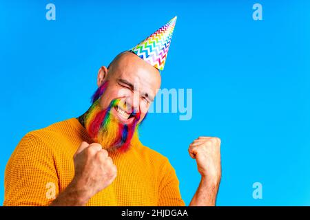 Fröhlicher Mann mit buntem Bart trägt Horn auf dem Kopf in blauem Studio-Hintergrund Stockfoto