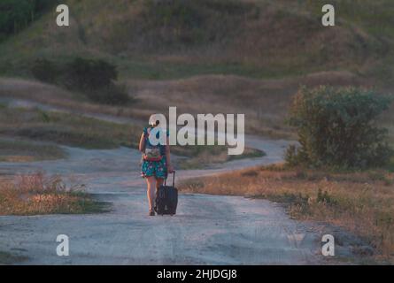 Mädchen mit Rucksack geht im Sonnenuntergang entlang der Straße Stockfoto