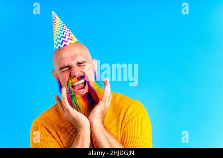 Fröhlicher Mann mit buntem Bart trägt Horn auf dem Kopf in blauem Studio-Hintergrund Stockfoto