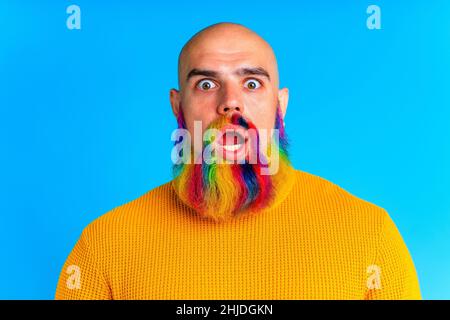 Cooler Mann mit buntem Bart, der die Kamera anschaut und sich im Studio-blauen Hintergrund fantastisch anfühlt Stockfoto