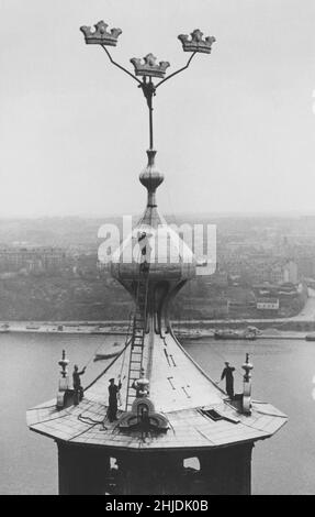 Stockholm im Jahr 1940s. Auf dem Dach des Stockholmer Rathauses werden Wartungsarbeiten durchgeführt. Ganz oben sind die schwedischen drei Kronen zu sehen, zusammen mit einem Arbeiter, der den ganzen Weg dorthin geklettert ist. Unter ihm sind Männer, die wahrscheinlich mit dem Metalldach arbeiten. Schweden 1949 Stockfoto