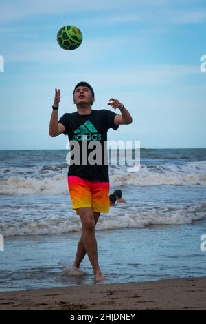 Palomino, Dibulla, La Guajira, Kolumbien - Dezember 4 2021: Ein junger Lateinmann mit bunten Shorts spielt mit einem Ball am Strand Stockfoto
