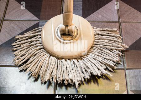 Ansicht des gebrauchten runden Wischmopps mit Mikrofaserkopf, braunem Griff auf Keramikfliesen. Stockfoto