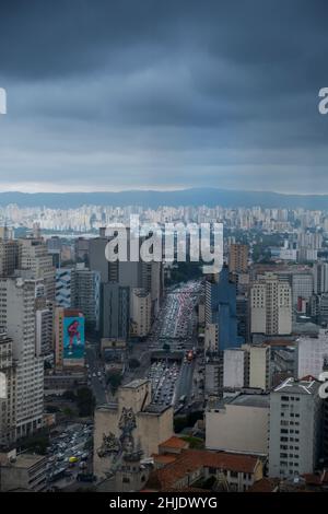 Brasilien, São Paulo. Erhöhter Blick auf den verstopften Verkehr auf der Prestes Maia Avenue und die massiven Hochhäuser im Stadtzentrum. Rauchige dunkelgraue Wolken. Stockfoto